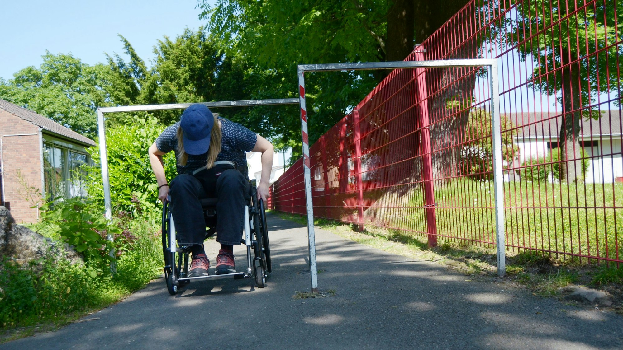 Eine Rollstuhlfahrerin duckt sich unter einem Umlaufgitter hindurch, um die Engstelle zu passieren.