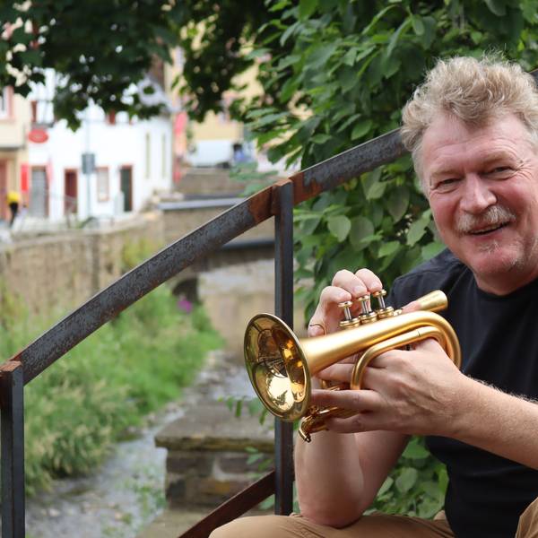 Hans Peter Salentin sitzt im Café Marielle in Bad Münstereifel auf einer rostigen Treppe, in seiner Hand hält er eine Mini-Trompete.