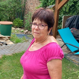 Katharina Willwerts steht in einem Garten. Hinter ihr ist ein Berg aus Holz.