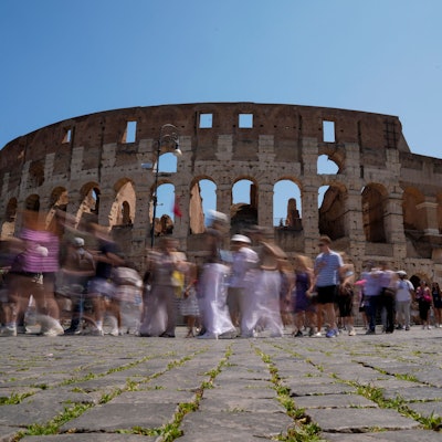 Touristen gehen am Kolosseum in Rom vorbei und machen Fotos.