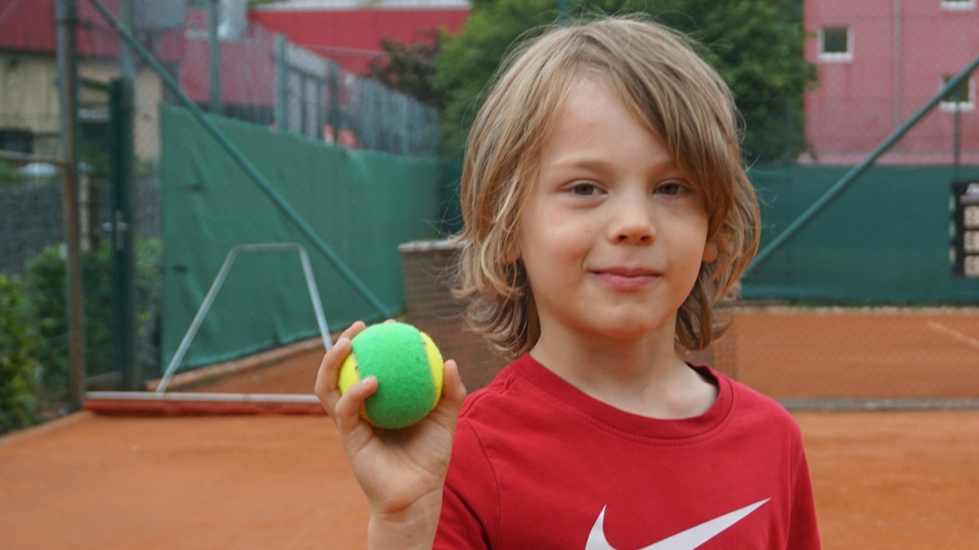 Ein Junge in einem roten T-Shirt hält einen grünen Tennisball.