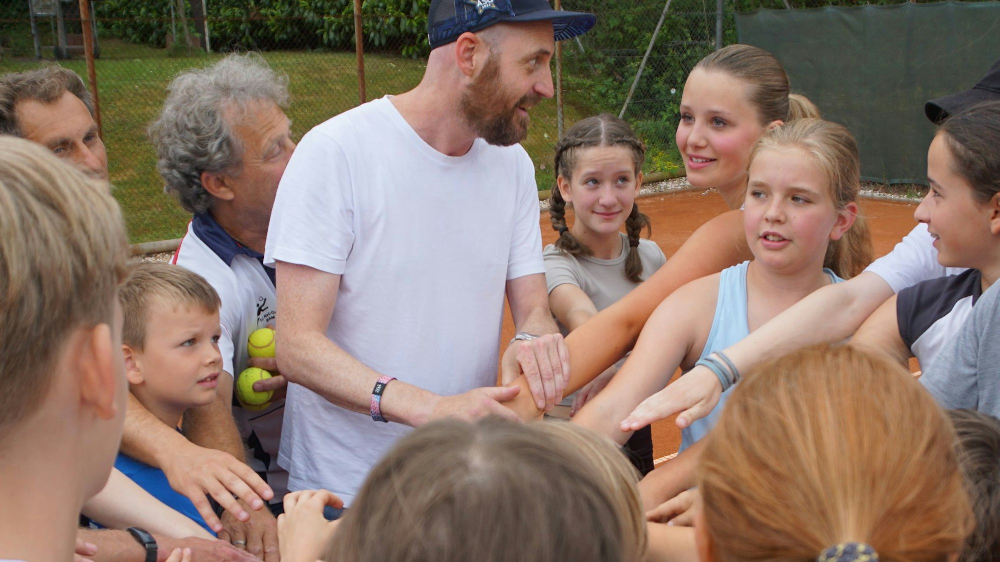 Die Kinder des TC Rot-Gold stehen auf dem Tennisplatz im Kreis. Sie stehen eng aneinander und halten ihre ausgestreckten Arme in die Mitte.