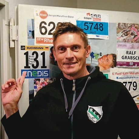 Ein Mann in Trainingsjacke vor einer Wand mit Startnummern.