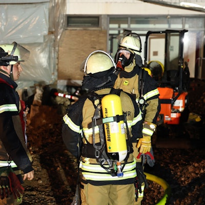 Drei Feuerwehrleute vor dem Eingang zur Turnhalle, vor dem ein Lüfter in Stellung gebracht wurde.