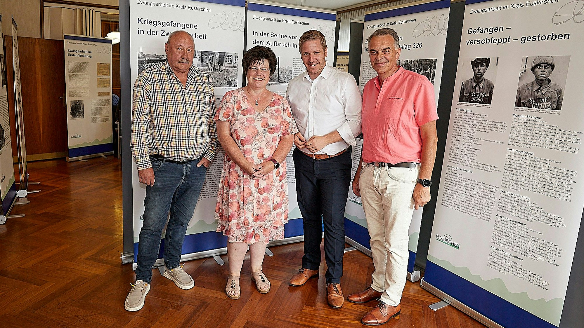 Drei Männer und eine Frau stehen vor den Stellwänden einer Ausstellung.