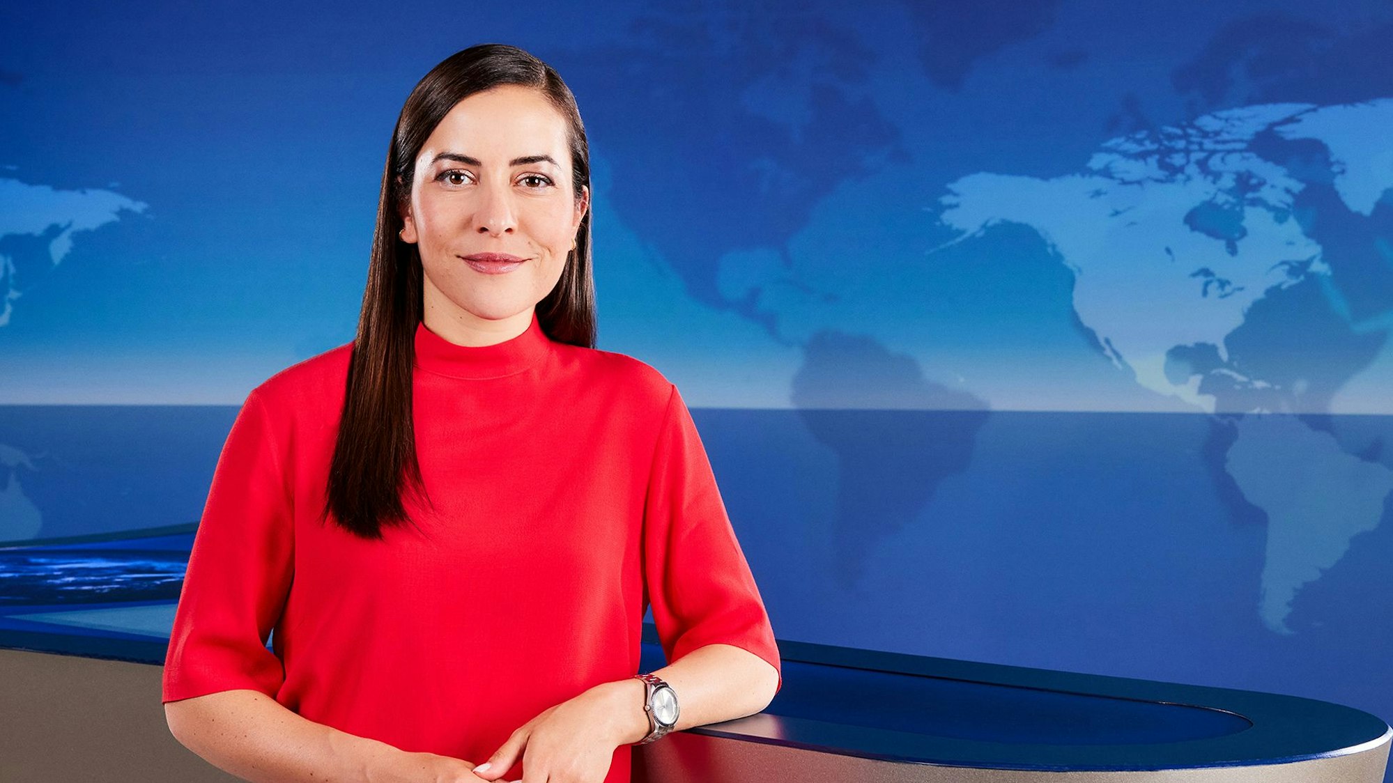 Aline Abboud, neue Moderatorin der „Tagesthemen“, steht im Nachrichtenstudio vor einer blauen Wand mit einer Weltkarte.