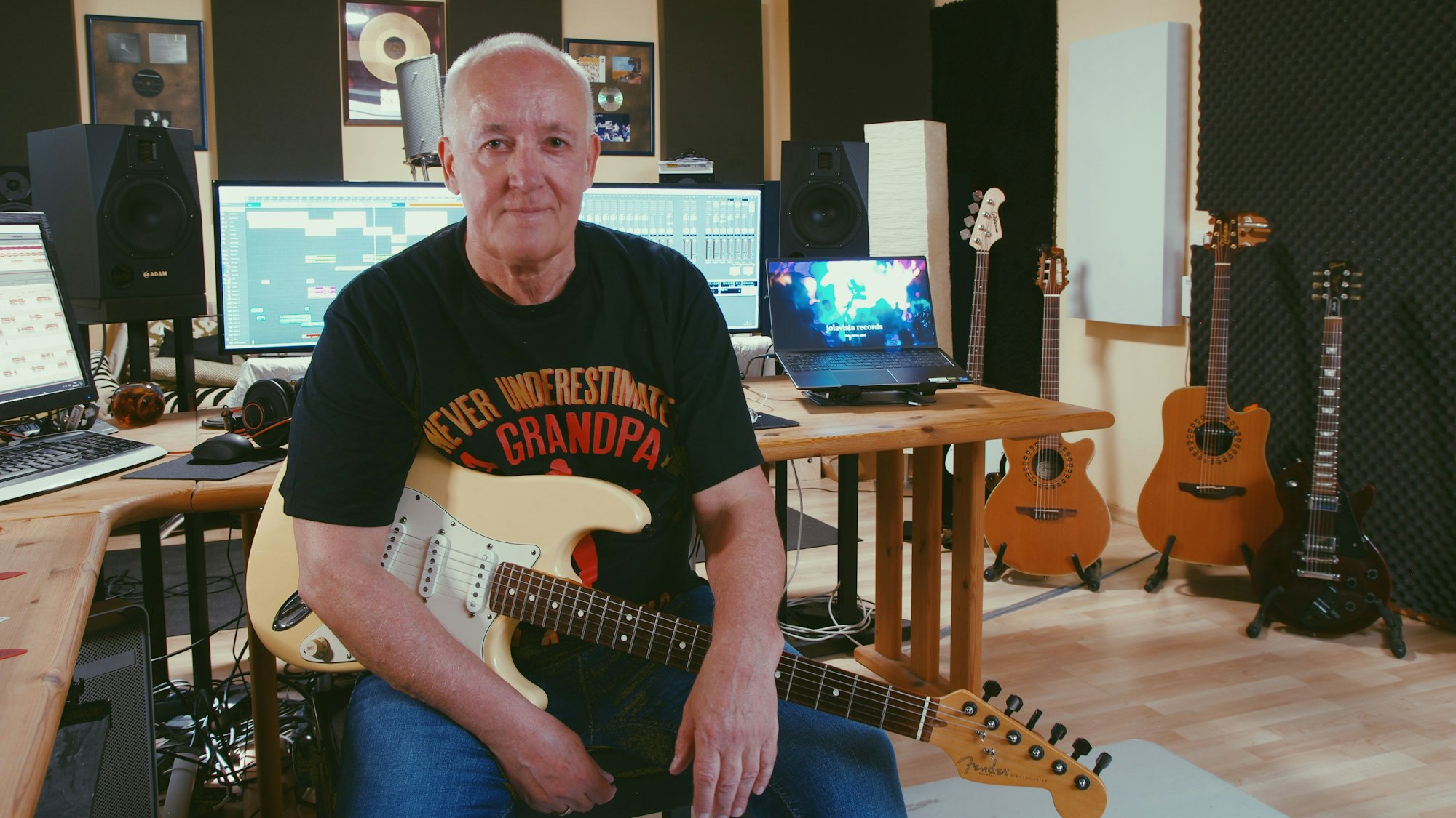 Der Musiker sitzt im Studio vor den digitalen Mischpulten, seine E-Gitarre hat er auf dem Schoß.