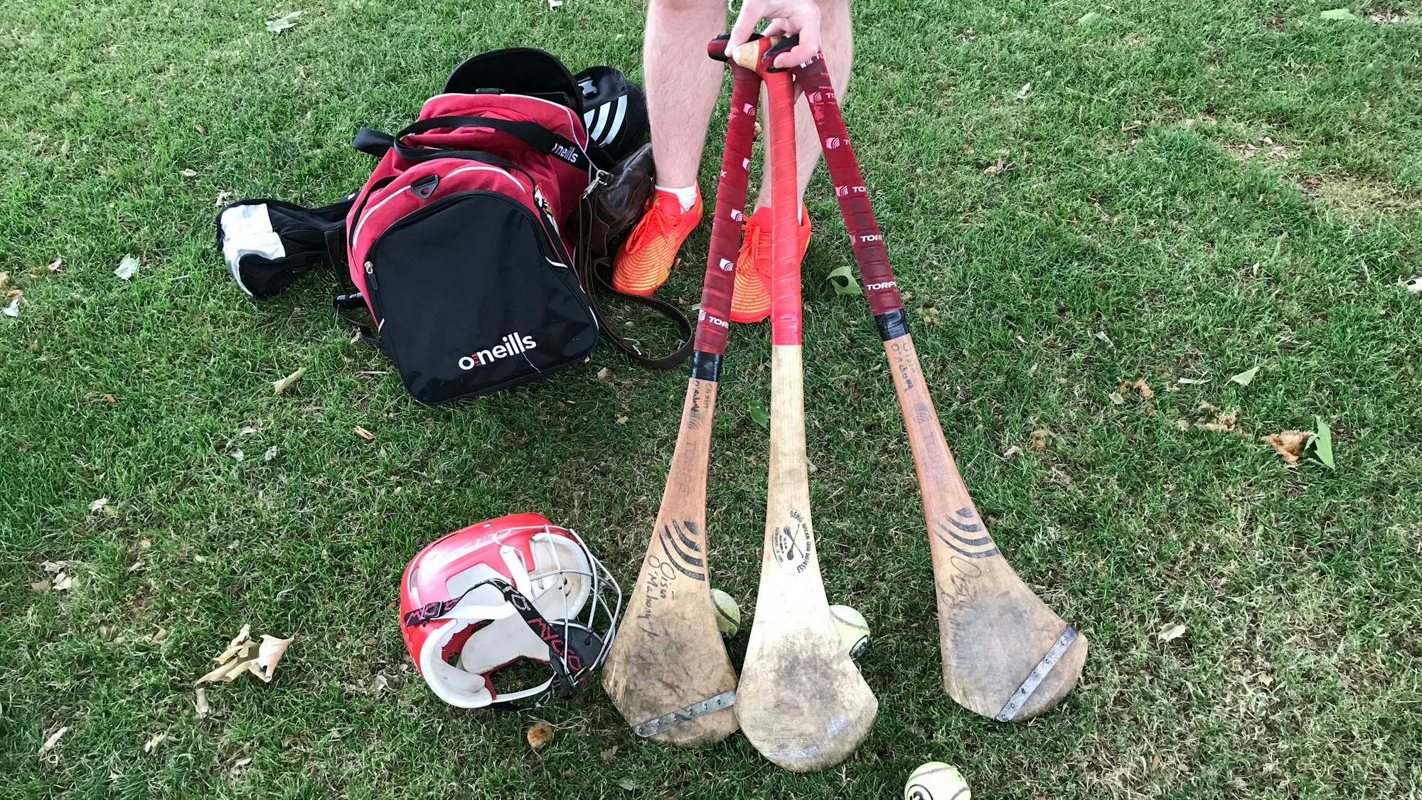 Drei Hurleys, also Schläger für das Hurling, ein Helm und eine Sporttasche liegen auf dem Rasen.