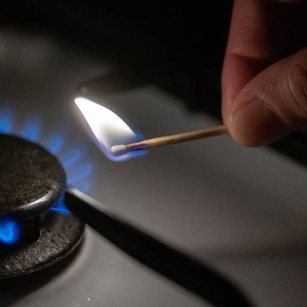 Eine Gasflamme wird auf einem Küchenherd mit einem Streichholz entzündet.
