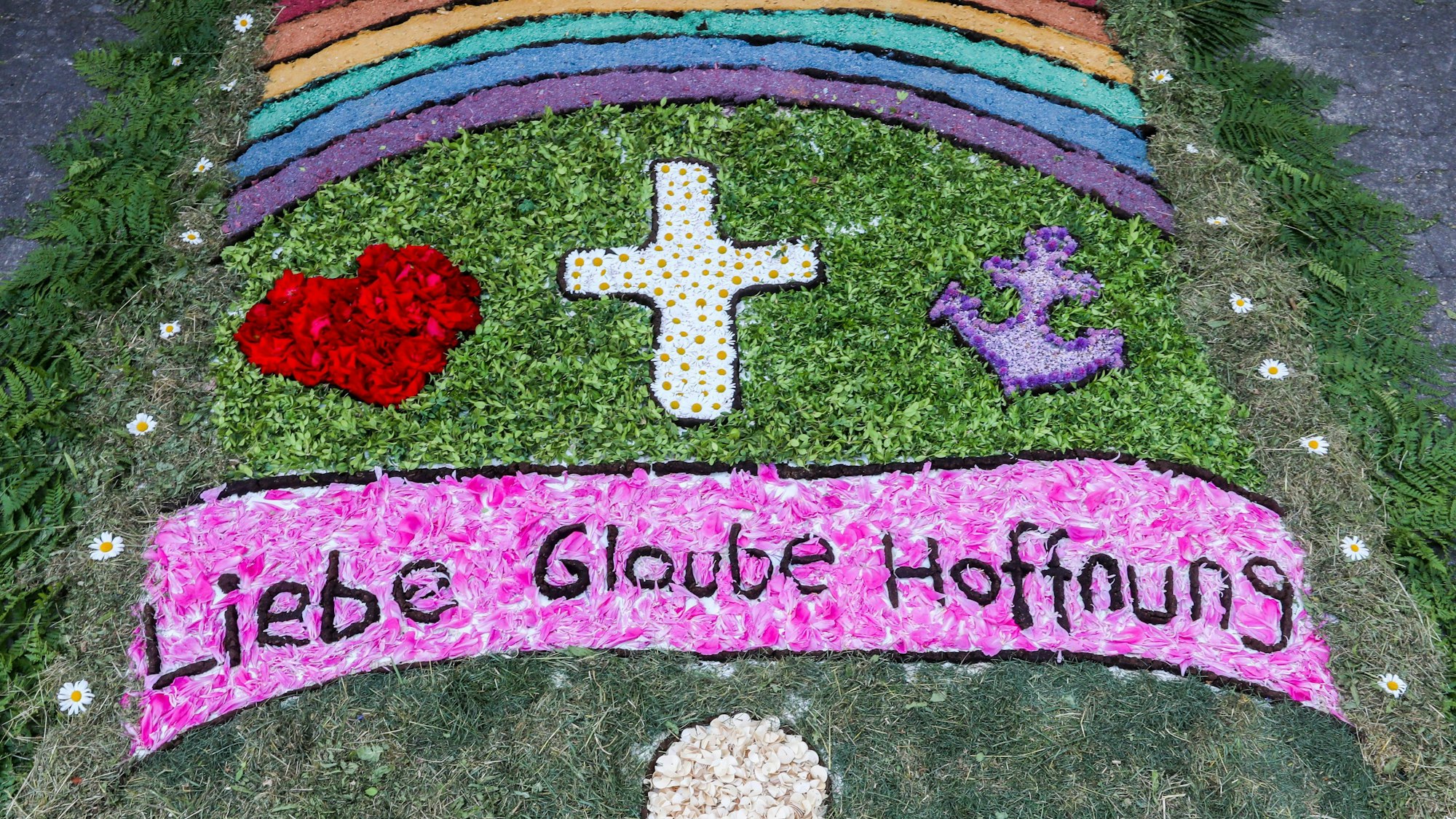 Die Wörter „Liebe, Glaube, Hoffnung“ sind zu lesen in einem Blumenteppich.