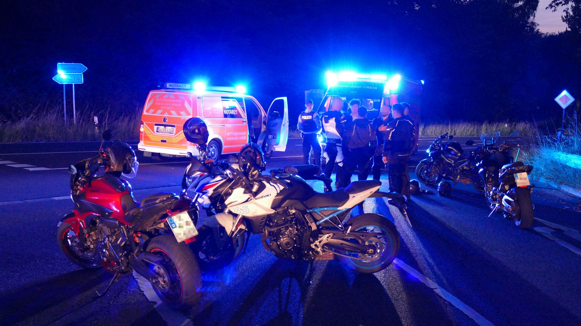 Motorräder einer Kolonne stehen an einer Kreuzung vor Polizei- und Rettungswagen.