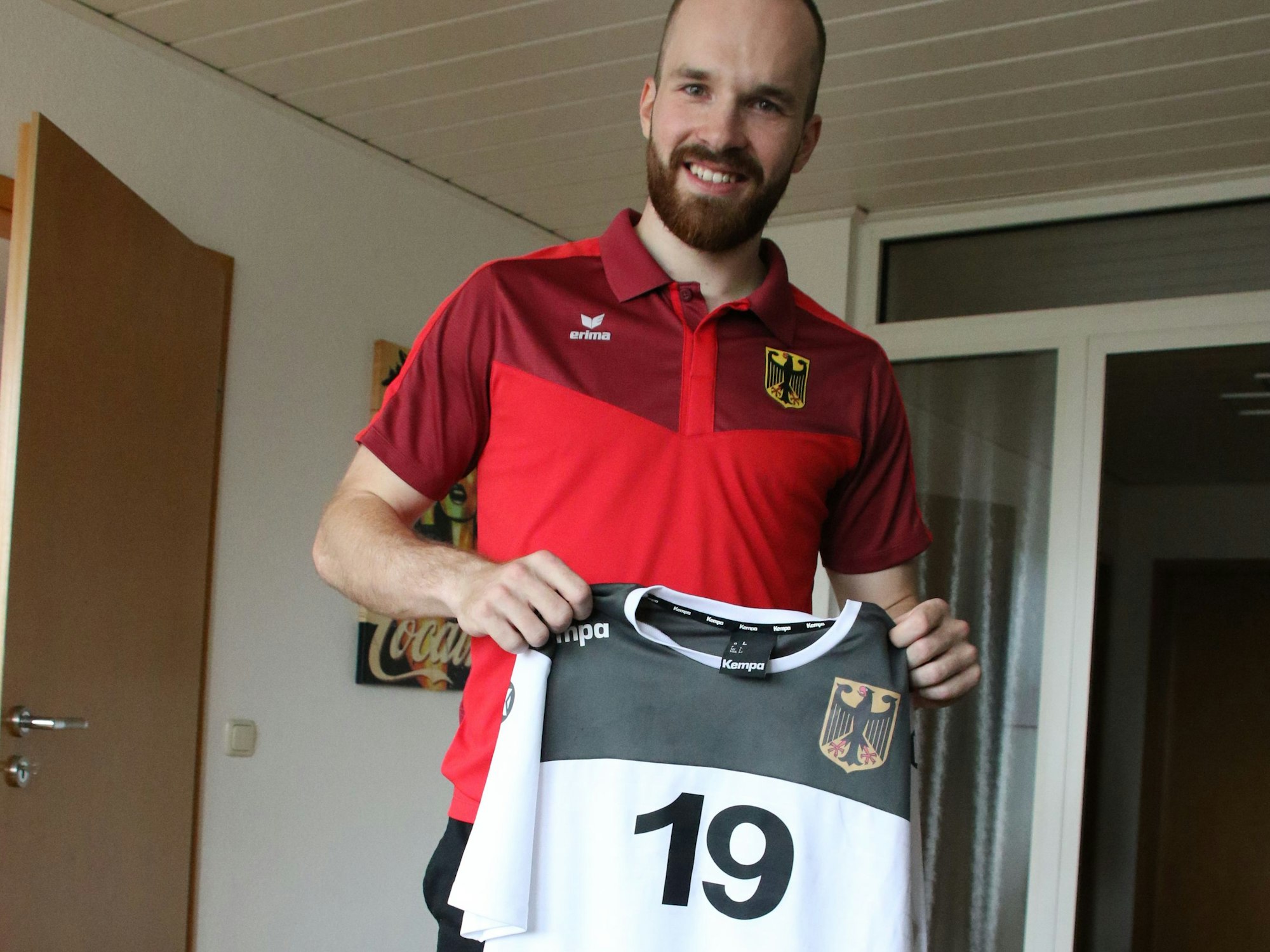 Simon Schöller im roten Deutschland-T-Shirt zeigt sein Trikot mit der Nr. 19.