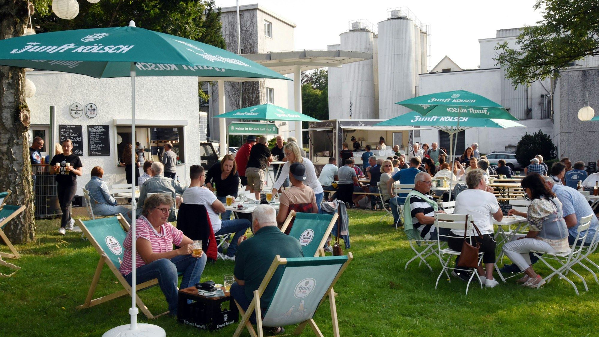 Der Biergarten mit Liegestühlen und Sonnenschirmen und den Brauerei-Gebäuden im Hintergrund.