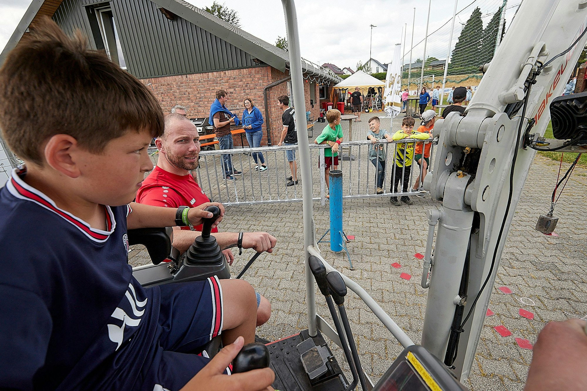 Ein Kind bedient mit den Joysticks einen Mini-Bagger, andere Kinder schauen zu.