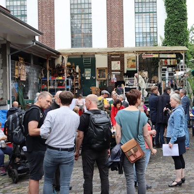Viele Menschen stehen auf dem Vorplatz eines fabrikartigen Gebäudes.