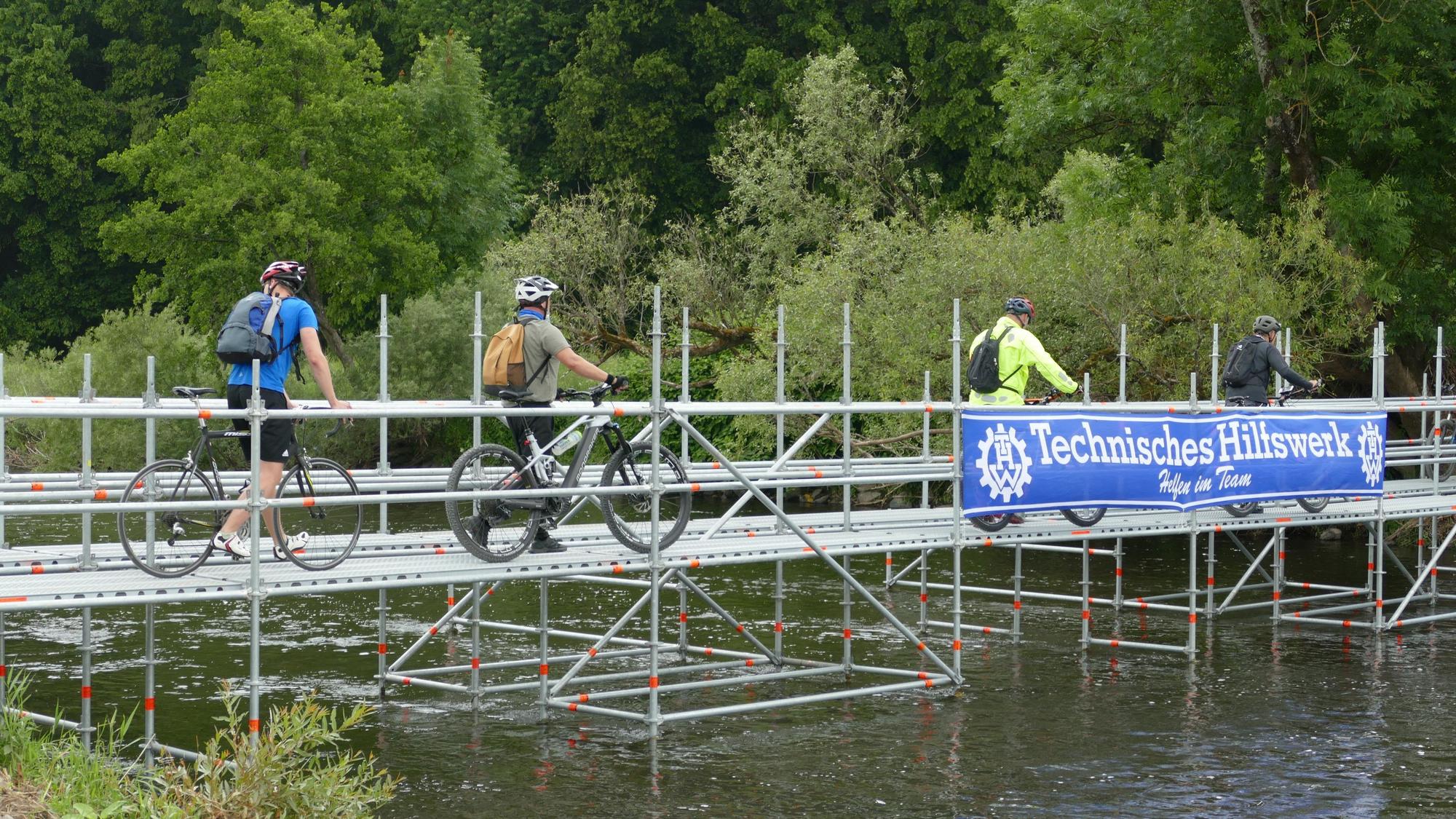 Fahrradfahrer fahren über eine provisorische Brücke.