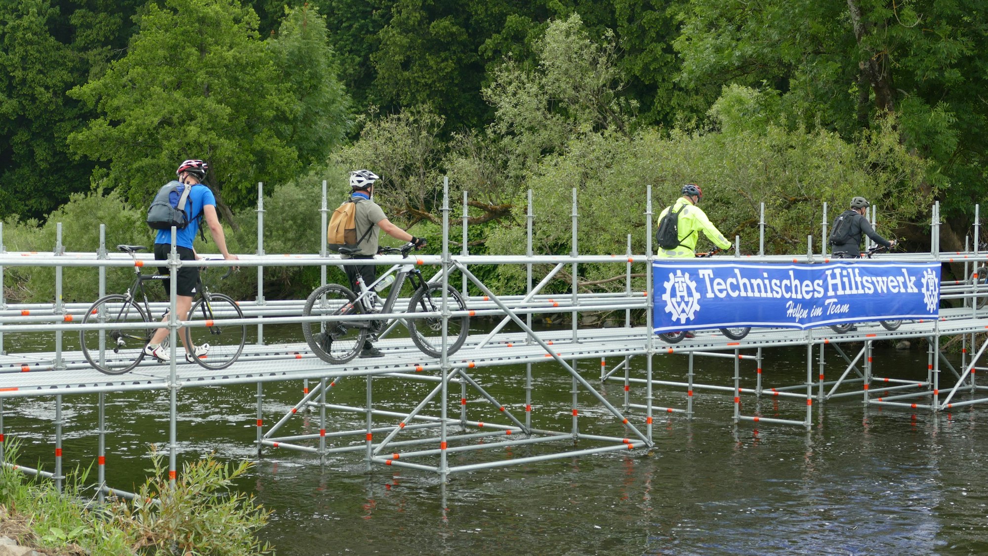 Das Bild zeigt eine provisorische Brücke über den Fluss Sieg, Radler fahren darüber.