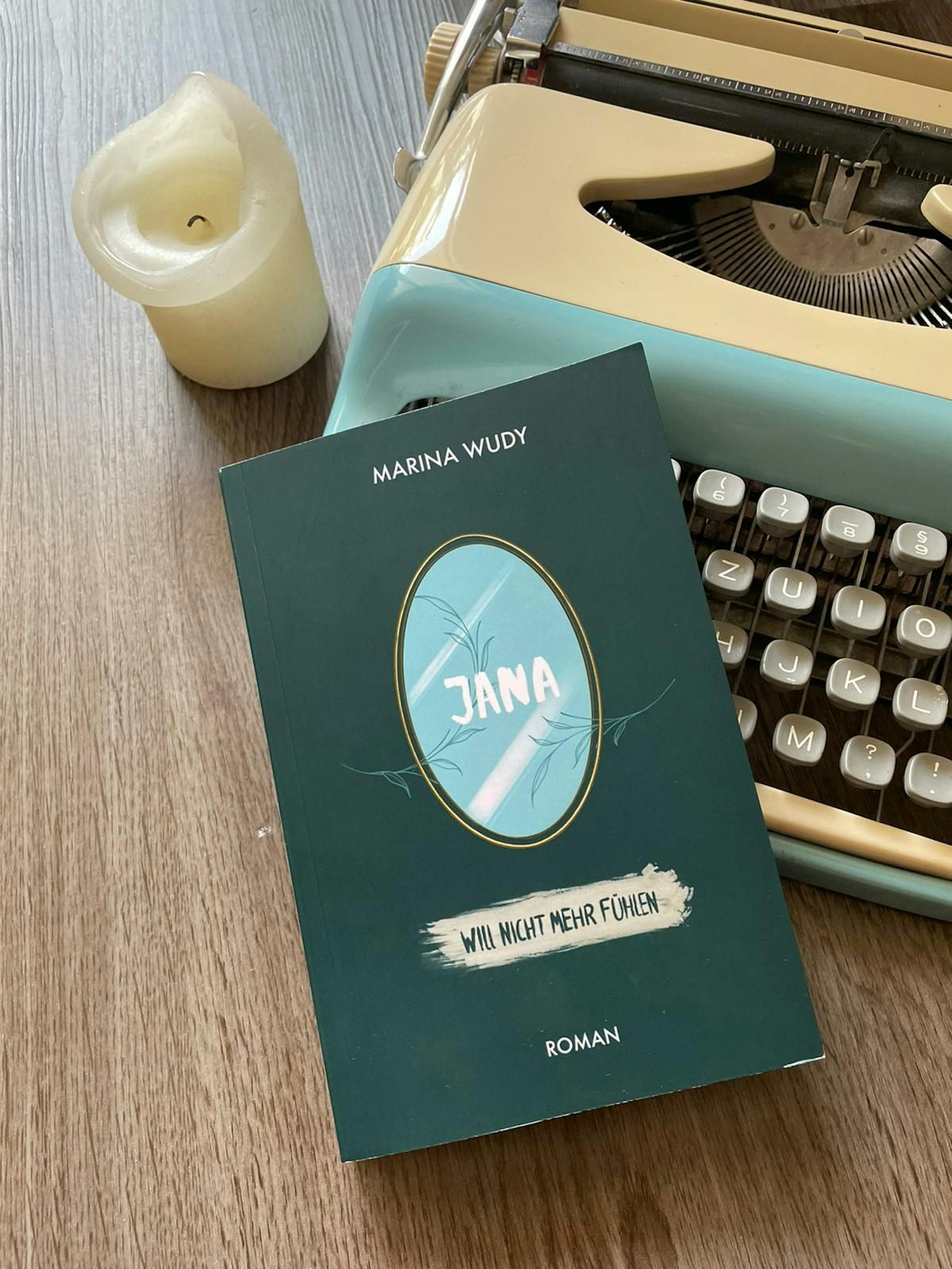 Ein grünes Buch liegt halb auf einer mintfarbenen Schreibmaschine.