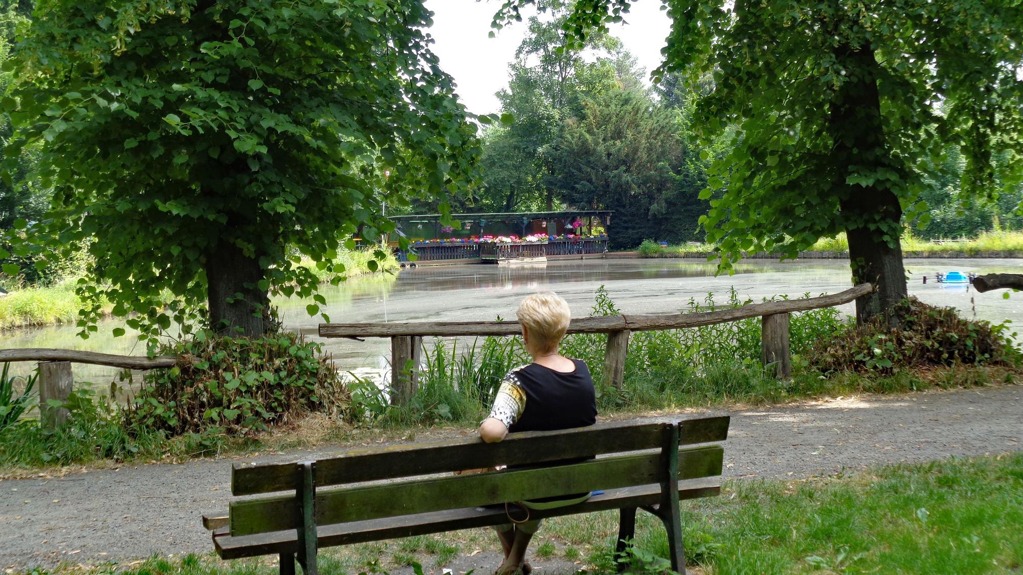 Eine Frau sitzt auf einer Bank am Teich.