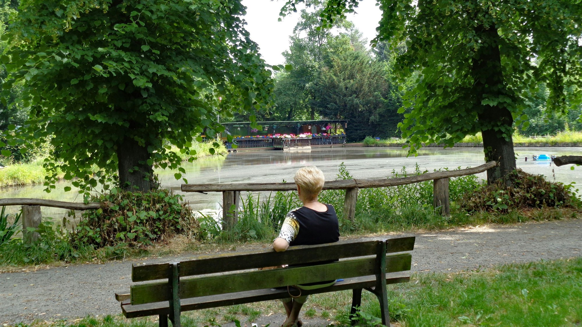 Eine Frau sitzt auf einer Bank am Teich.
