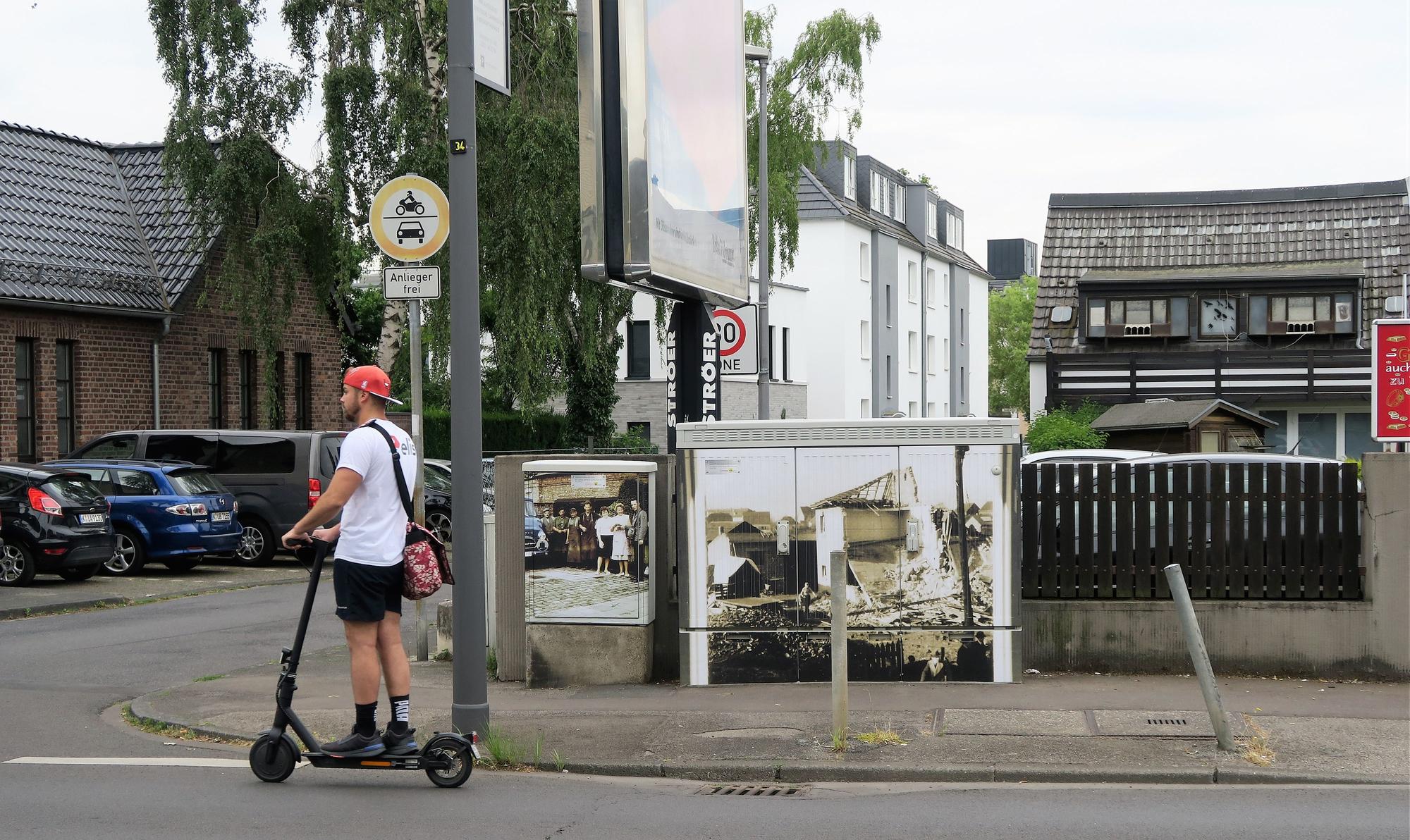 Ein historisches Motiv prangt auf einem Stromkasten. Ein Mann auf einem Elektroroller fährt gerade daran vorbei.