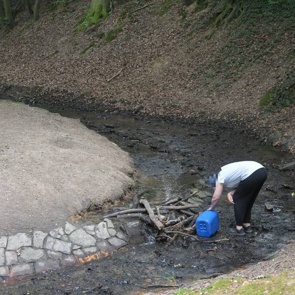 Eine Person entnimmt illegal Wasser aus dem Milchbornbach. In der Hand hält sie einen blauen Kanister.