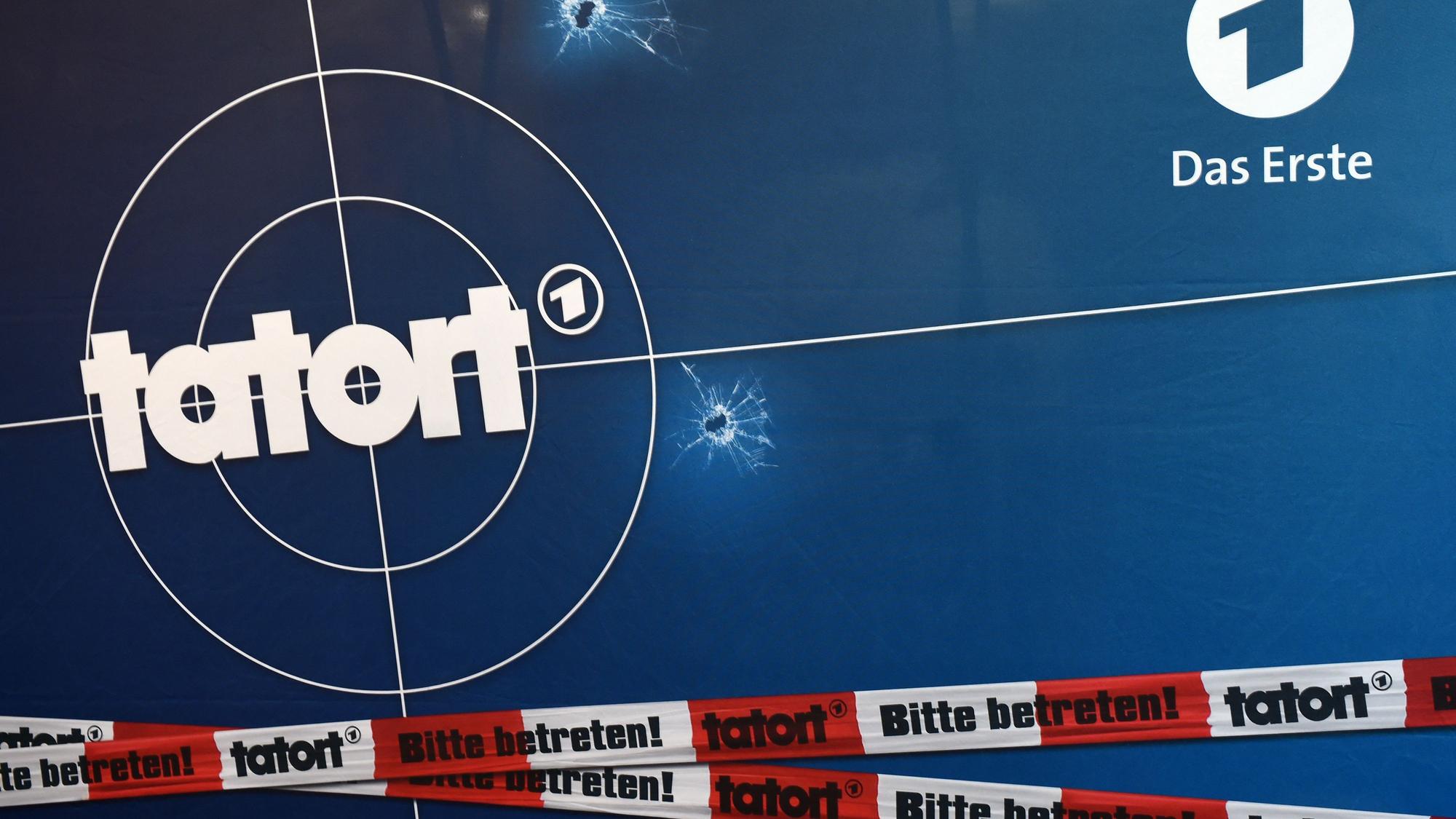 Auf einer Fotorückwand sind das Logo der ARD-Fernsehreihe „Tatort“ zu sehen, zudem ein rot-weißes Absperrband.