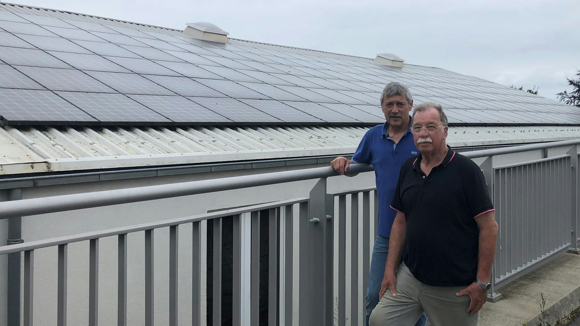 Zwei Männer vor einem Haus, auf dessen Dach Solarmodule sind.
