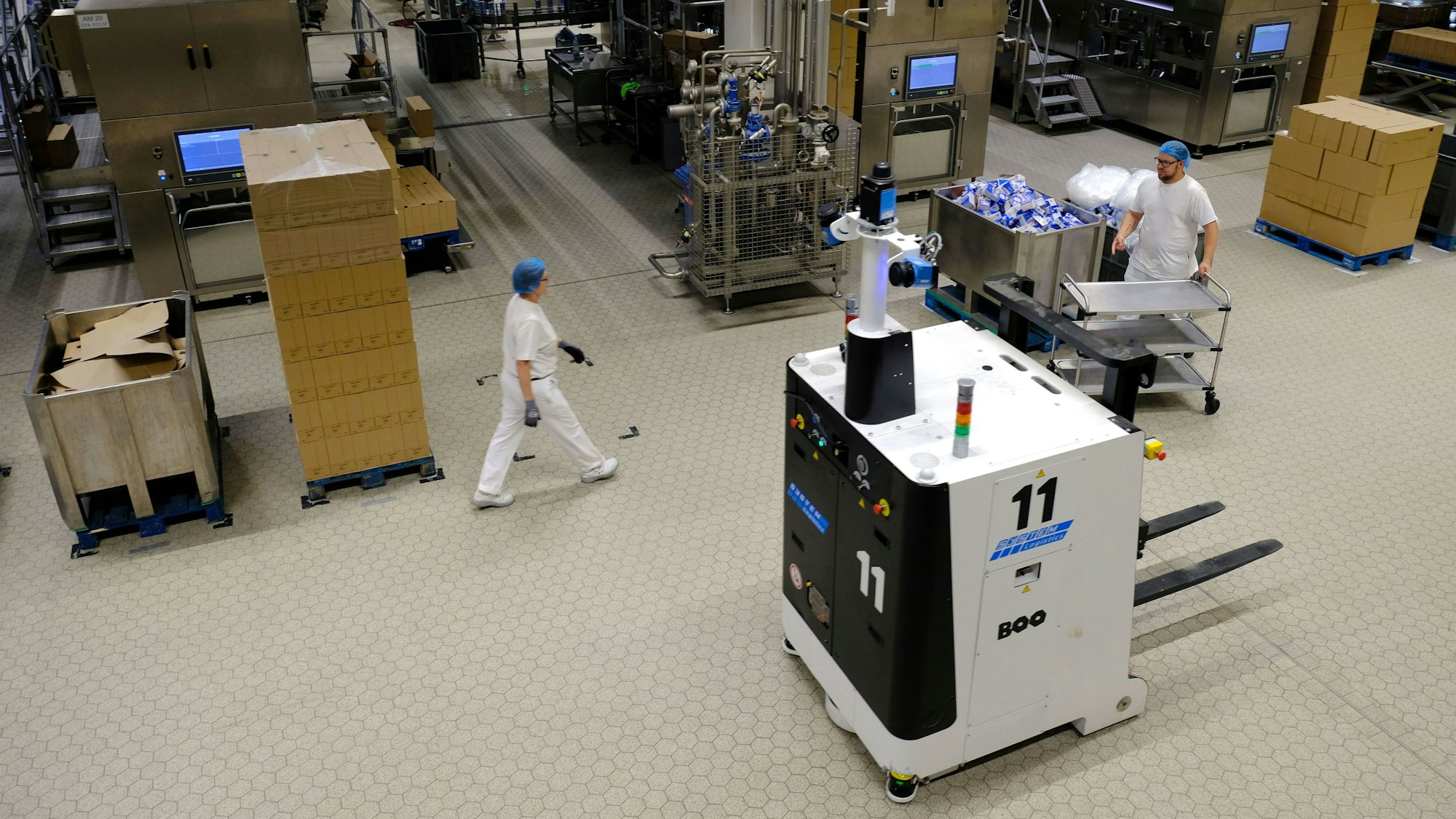 Zwei Molkerei-Mitarbeitende und ein autonomes Förderfahrzeug in einer Produktionshalle.