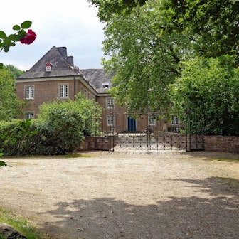 Die Burg Bachem in Frechen, umgeben von Grün und Rosenbüschen.