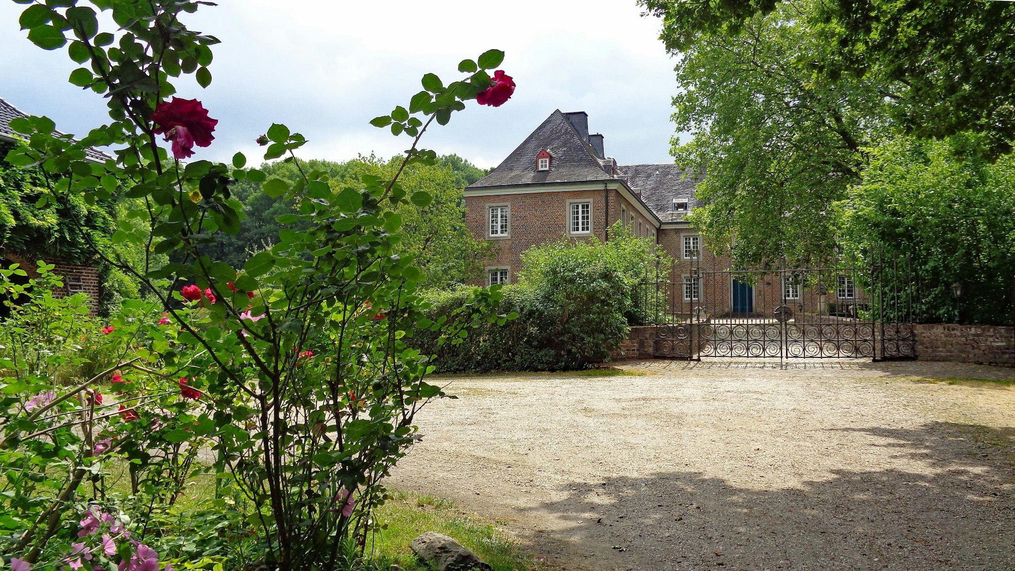 Die Burg Bachem in Frechen, umgeben von Grün und Rosenbüschen.