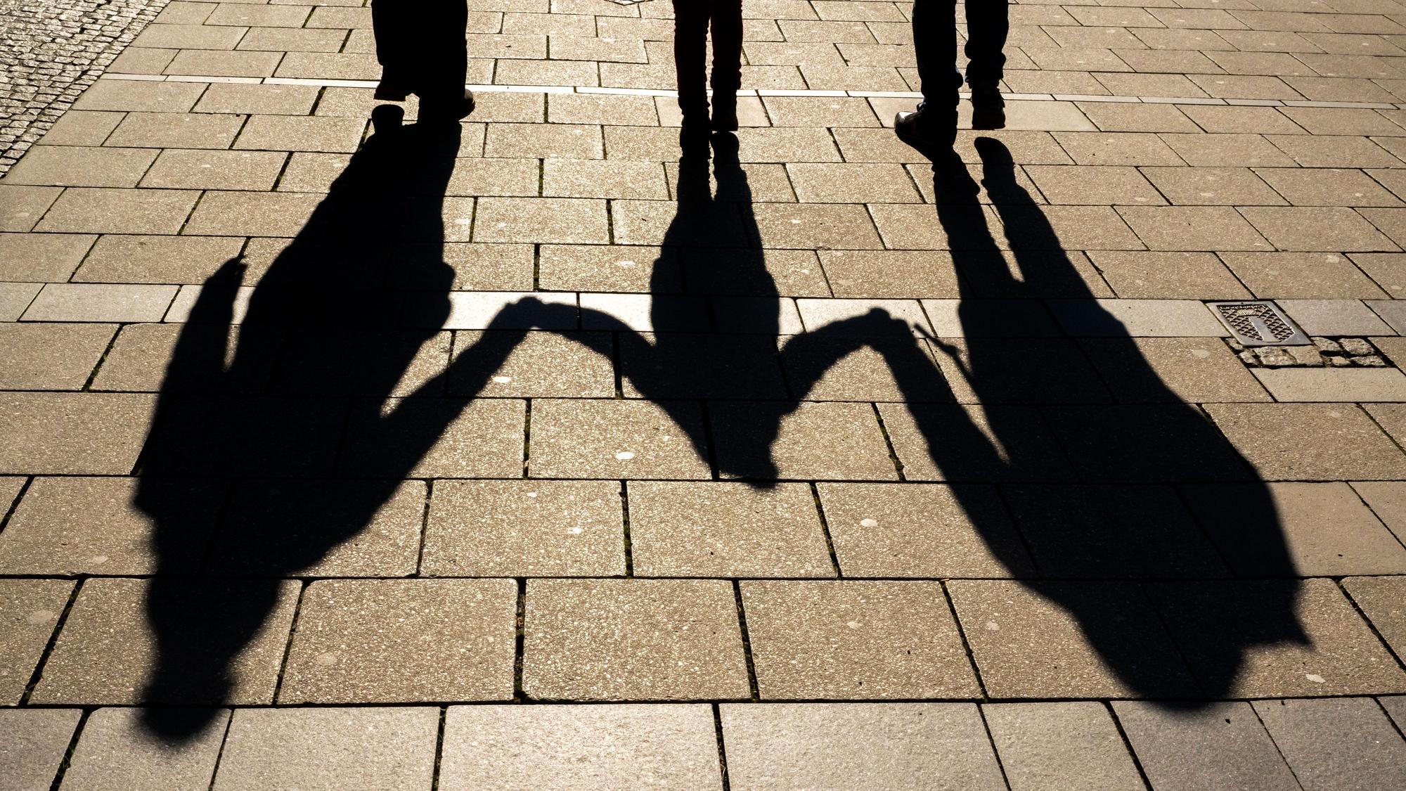 Die Schatten von zwei Erwachsenen und einem Kind fallen in den Morgenstunden auf den Asphalt.