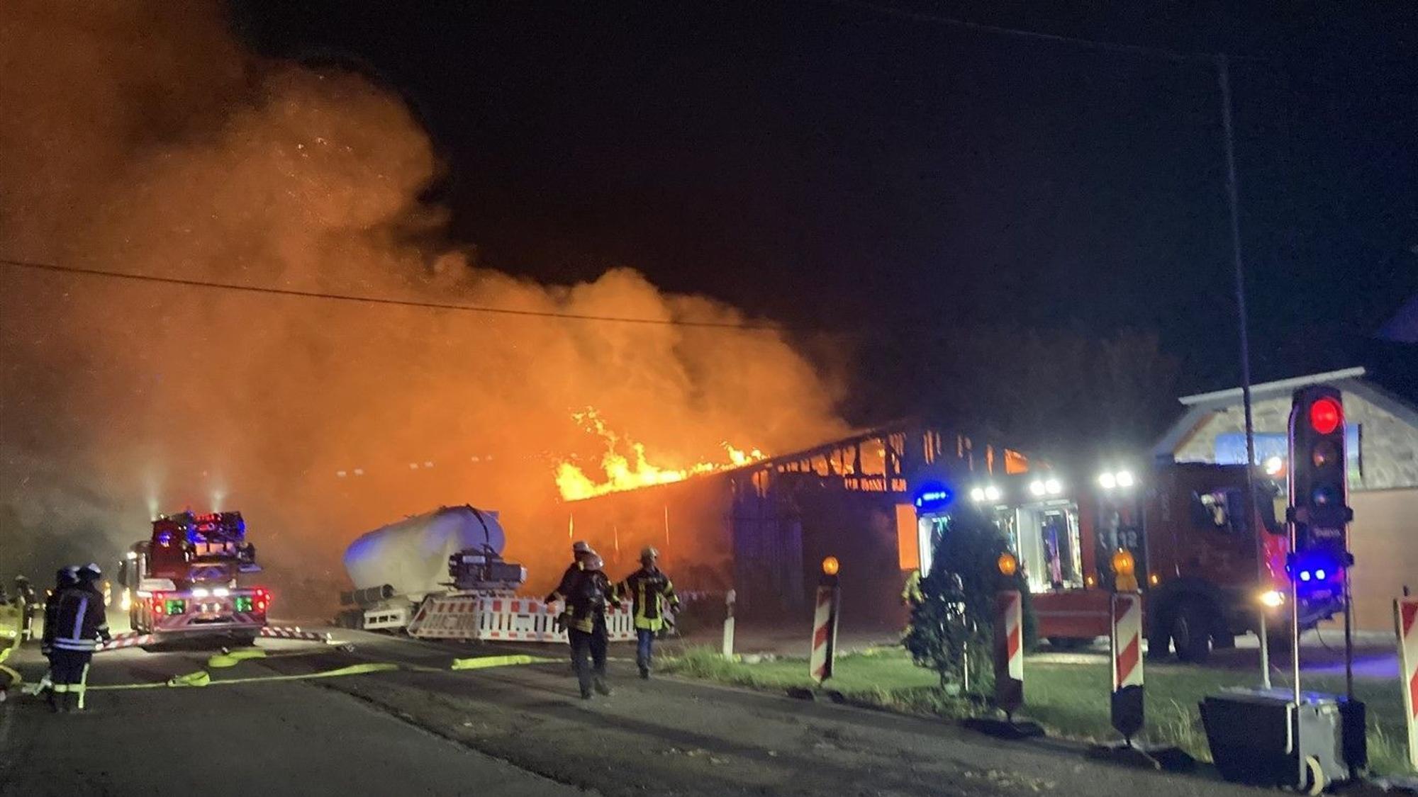 Eine Scheune brennt bei Nacht. Rauch steigt auf. Feuerwehrmänner sind im Einsatz.