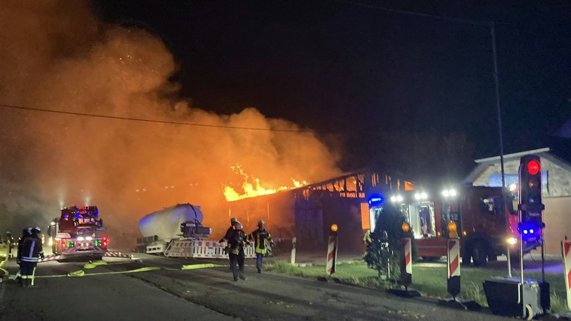 Eine Scheune brennt bei Nacht. Rauch steigt auf. Feuerwehrmänner sind im Einsatz.