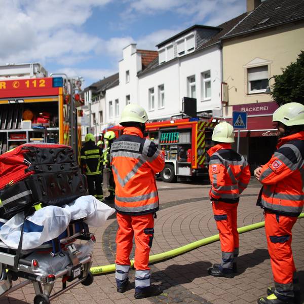Rettungskräfte stehen vor einem Gebäude auf einer Straße.