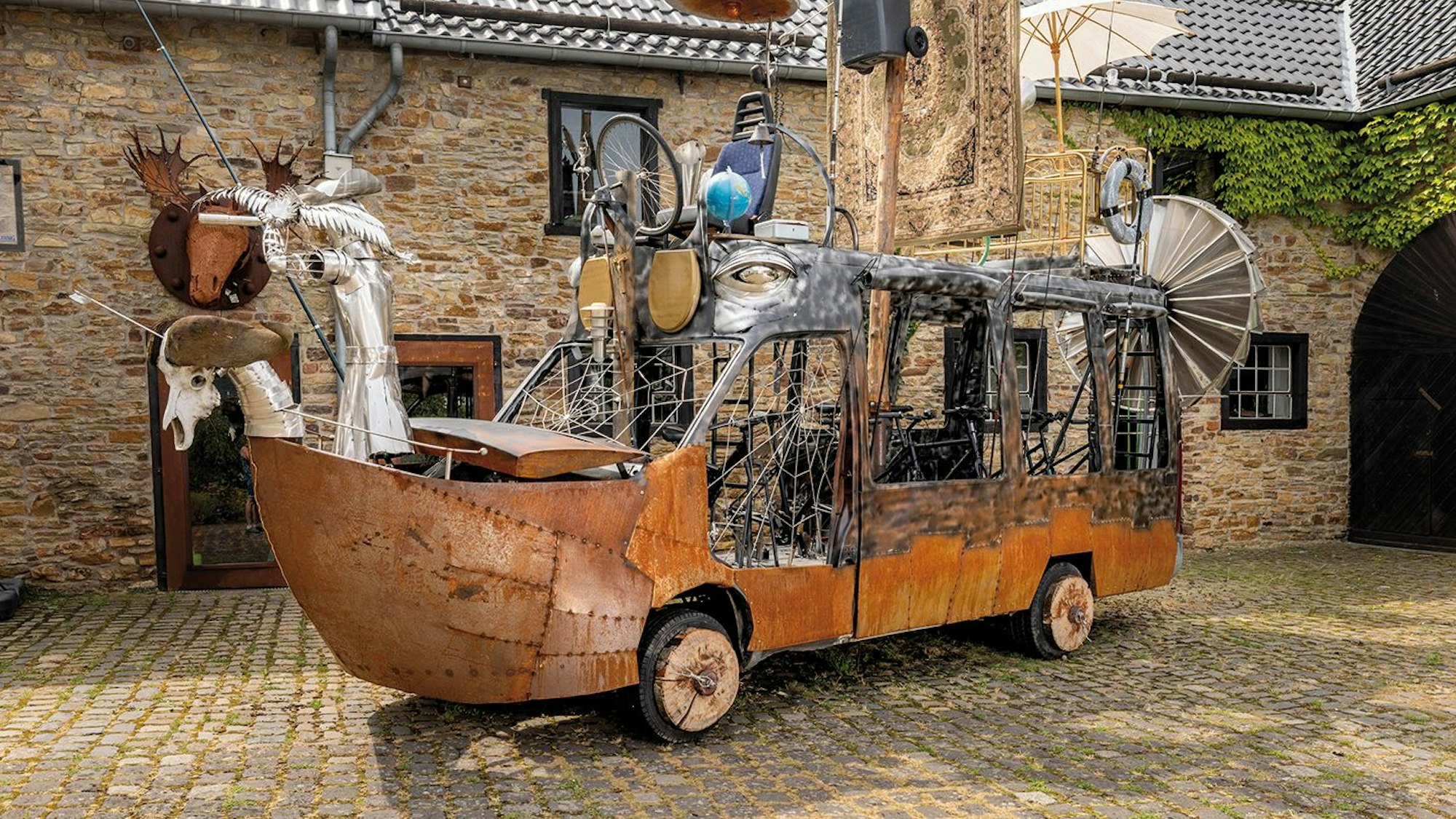 Das Foto zeigt ein aus Schrott und Abfall gebautes Kunstobjekt auf Rädern.