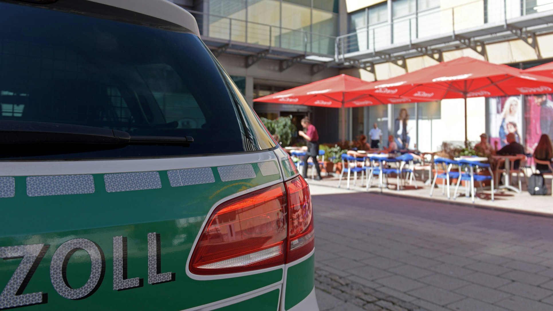 Vor einem Straßencafé steht ein Streifenwagen des Zolls.