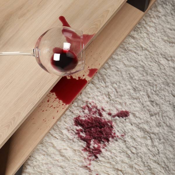 Ein verschüttetes Glas Rotwein auf weißem Teppich.