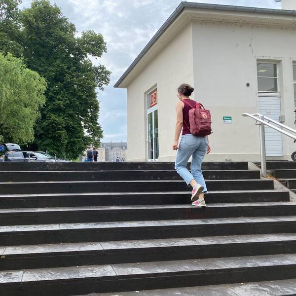 Eine Frau steigt die Treppe zum Bahnhofsvorplatz hinauf. Im Hintergrund ist das Schloss Augustusburg zu sehen.