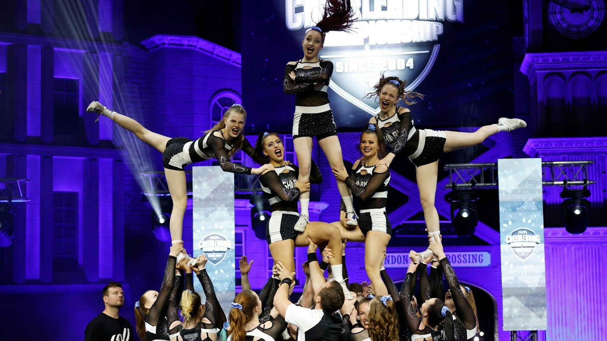 Ein Cheerleader-Team steht als menschliche Pyramide auf der Bühne.