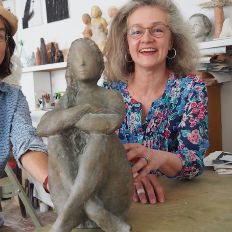 Die beiden Künstlerinnen lächeln in die Kamera – in ihrer Mitte sitzt die Plastik.