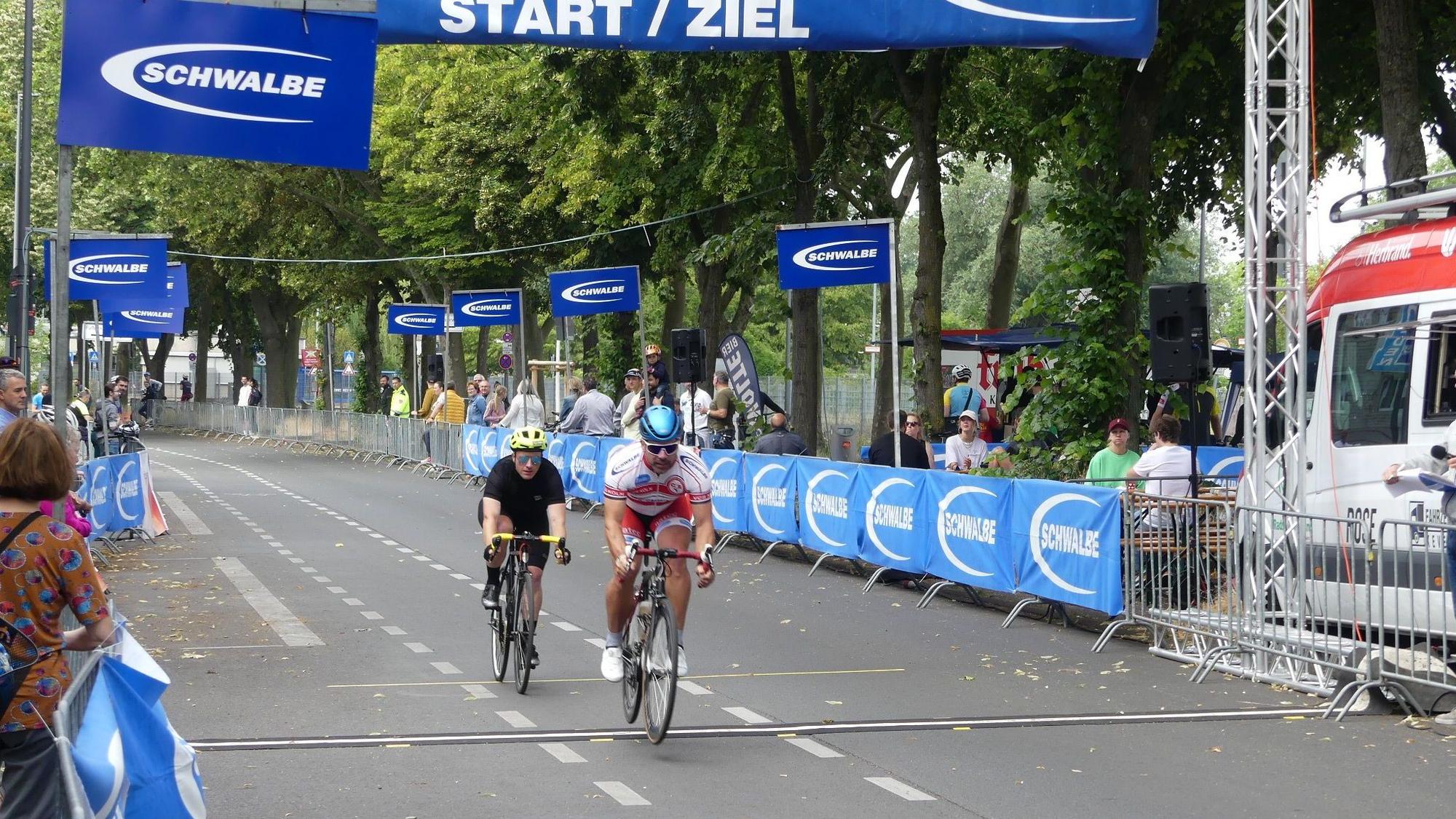 Zwei Radrennfahrer überqueren knapp hintereinander die Ziellinie.