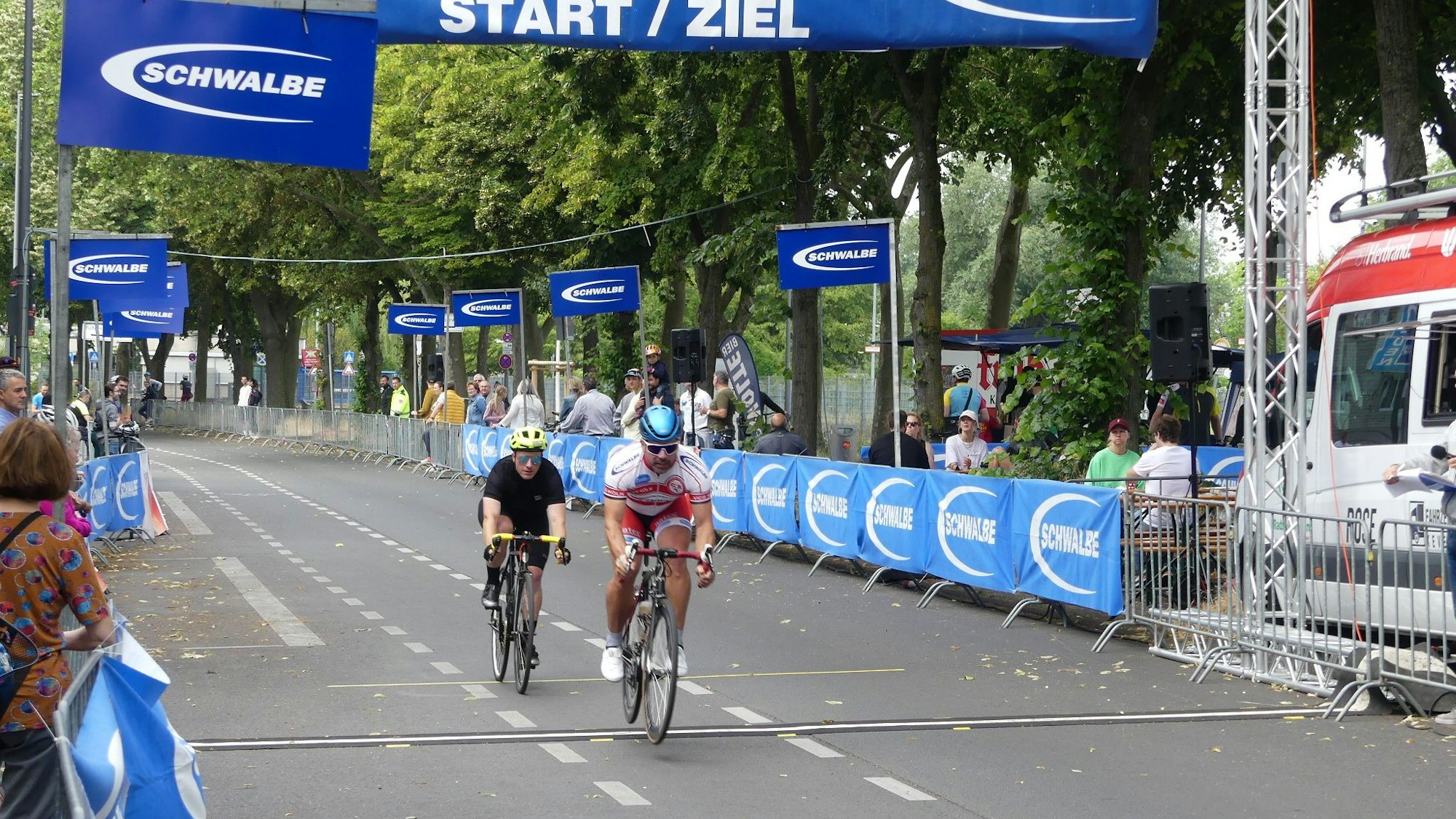 Zwei Radrennfahrer überqueren knapp hintereinander die Ziellinie.