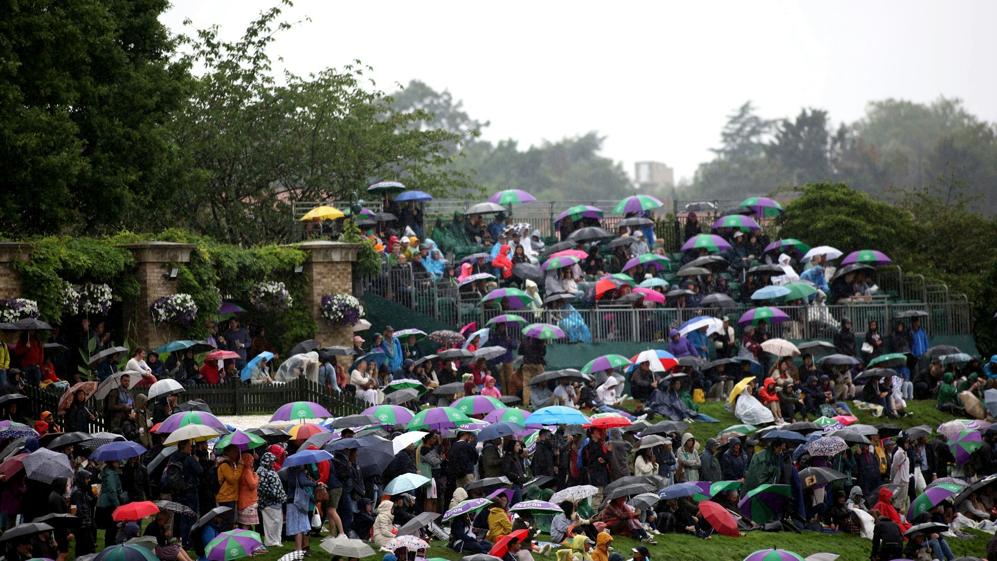 Zuschauer suchen am zweiten Tag der Tennismeisterschaften in Wimbledon Schutz vor dem Regen.