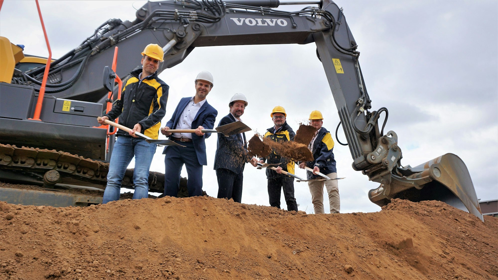 Ein Bagger steht im Hintergrund. Davor fünf Männer mit Schaufeln: Michael Merten, Abteilungsleiter der Niederlassung Betrieb Bonn (v.l.); Wolfgang Honecker, technischer Beigeordneter; Elmar Müller, Wirtschaftförderer der Stadt Euskirchen; Peter Mayer, regionaler polit. Beauftragter dt. Post; Michael Neußer, Betriebsratsvorsitzender Bonn