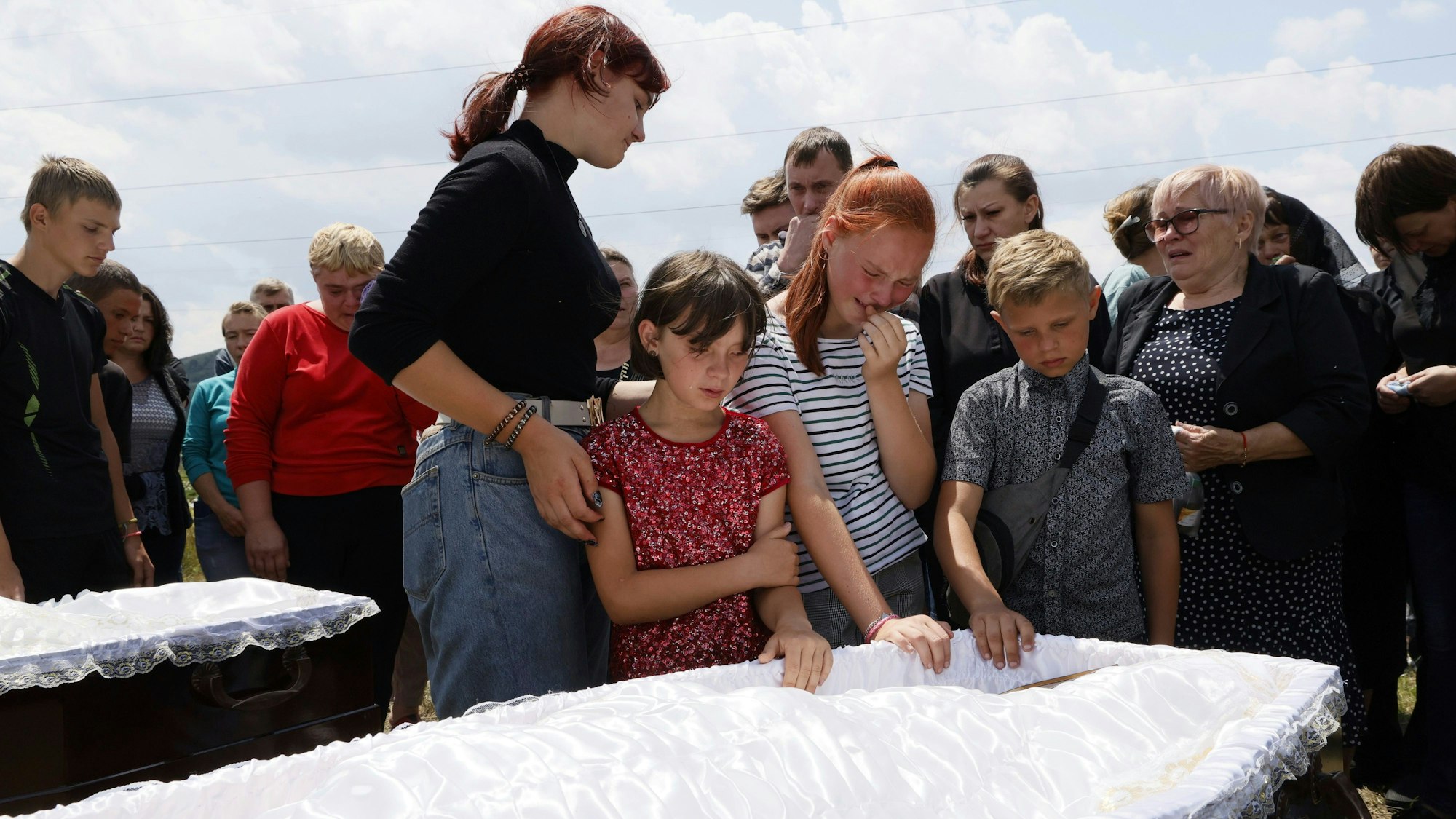 Kinder stehen vor einem Sarg und weinen.