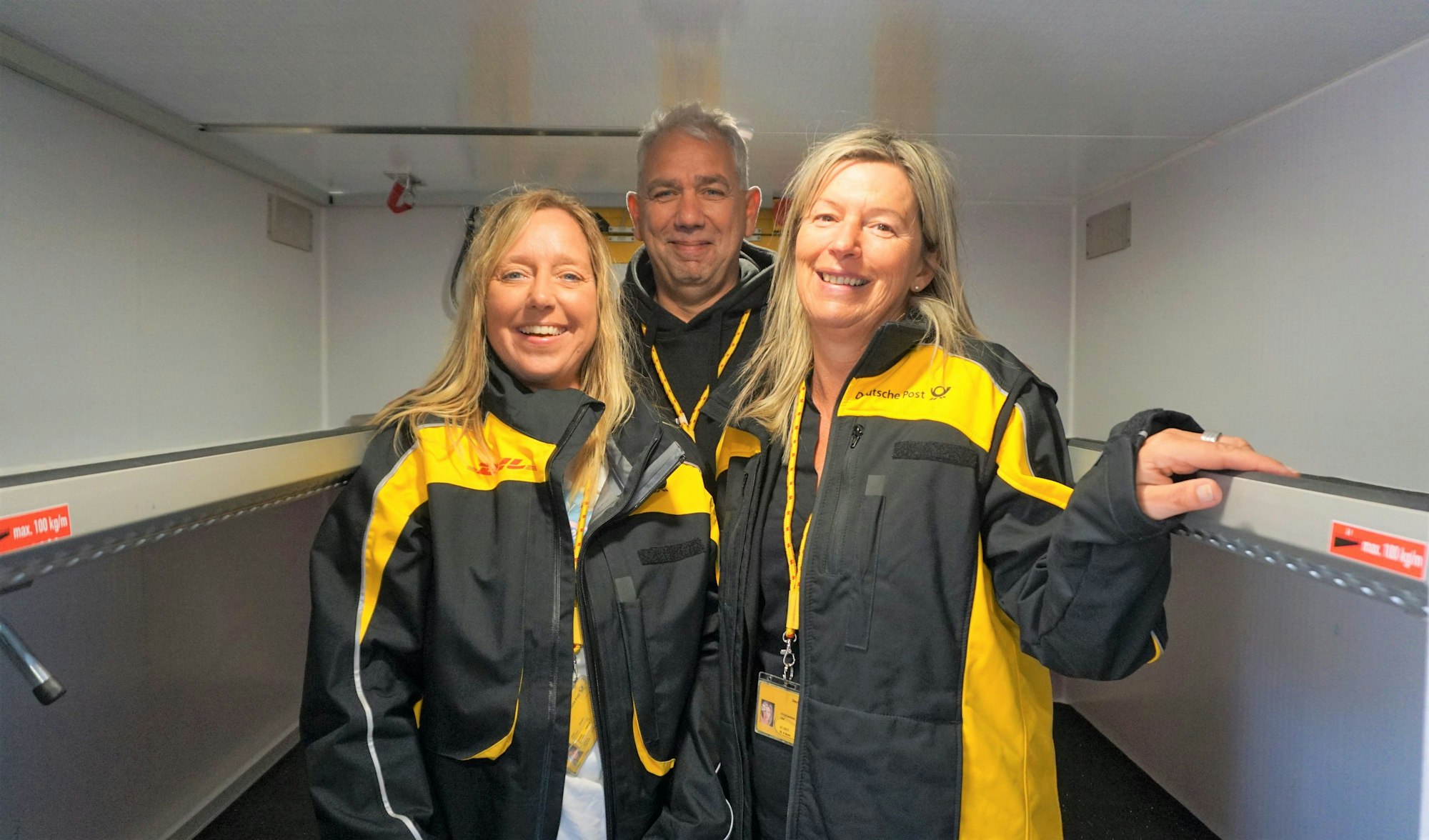 In einem elektrisch betriebenem Postwagen stehen Sabine Kresen, Standortleitung Bad Münstereifel; Roland Strick, Standortleiter Euskirchen und Ute Klinkhammer Zustellstützpunktleiterin Euskirchen in Jacken der Deutschen Post.