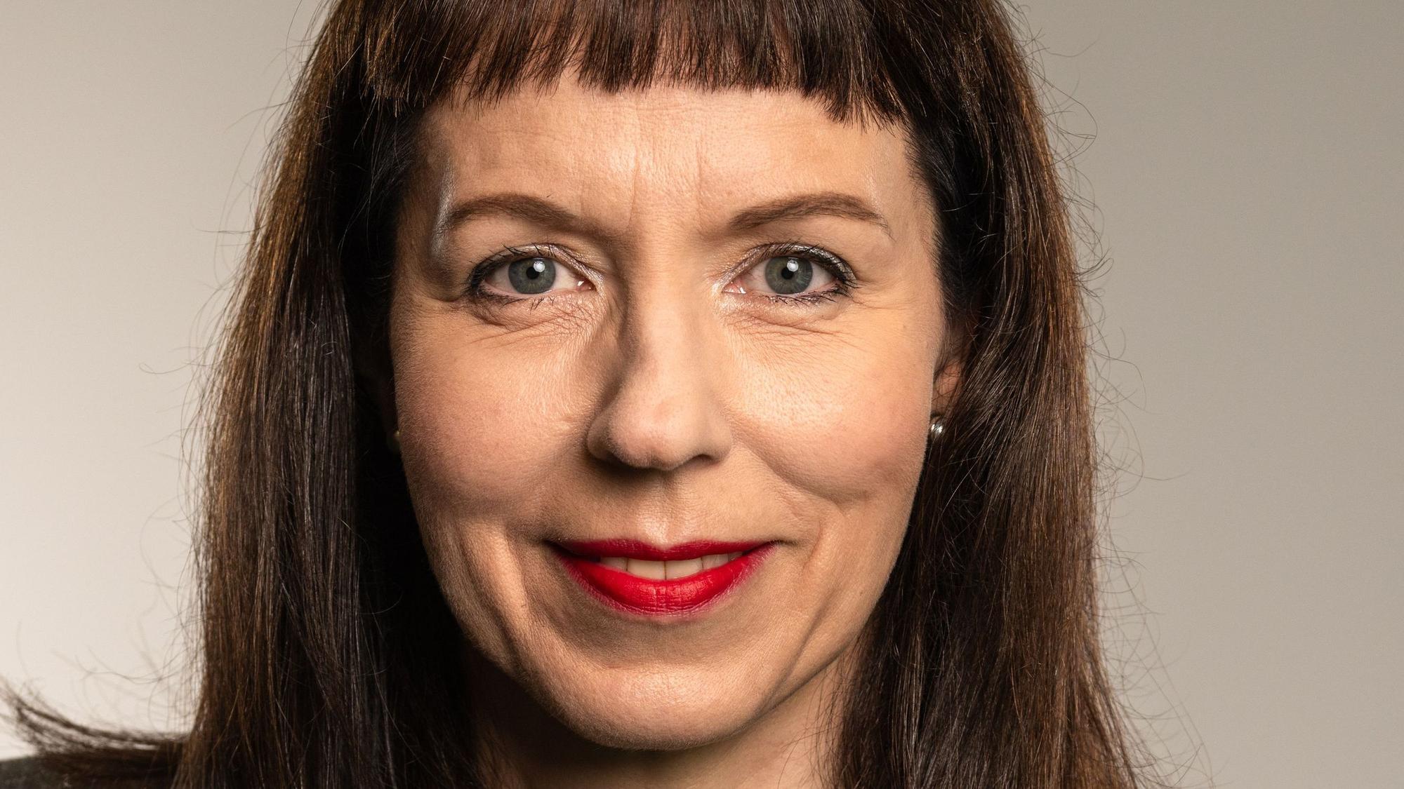 Ein Porträtfoto von Gisela Eichler. Sie hat schulterlange dunkle Haare mit Pony, trägt roten Lippenstift und guckt freundlich.