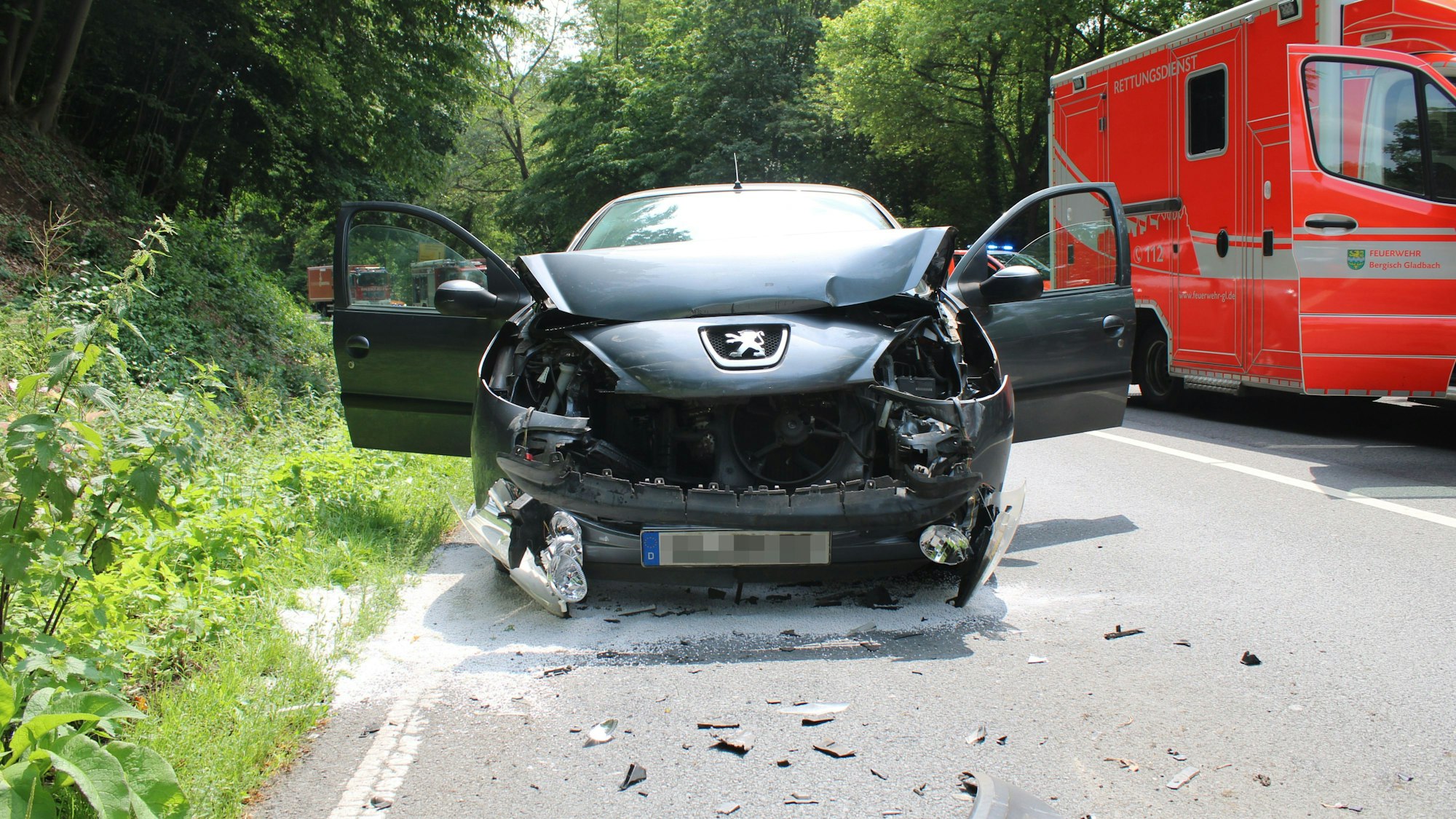 Ein Auto steht mit zerbeulter Front auf der Straße, die Türen stehen offen. Daneben ein Rettungswagen.