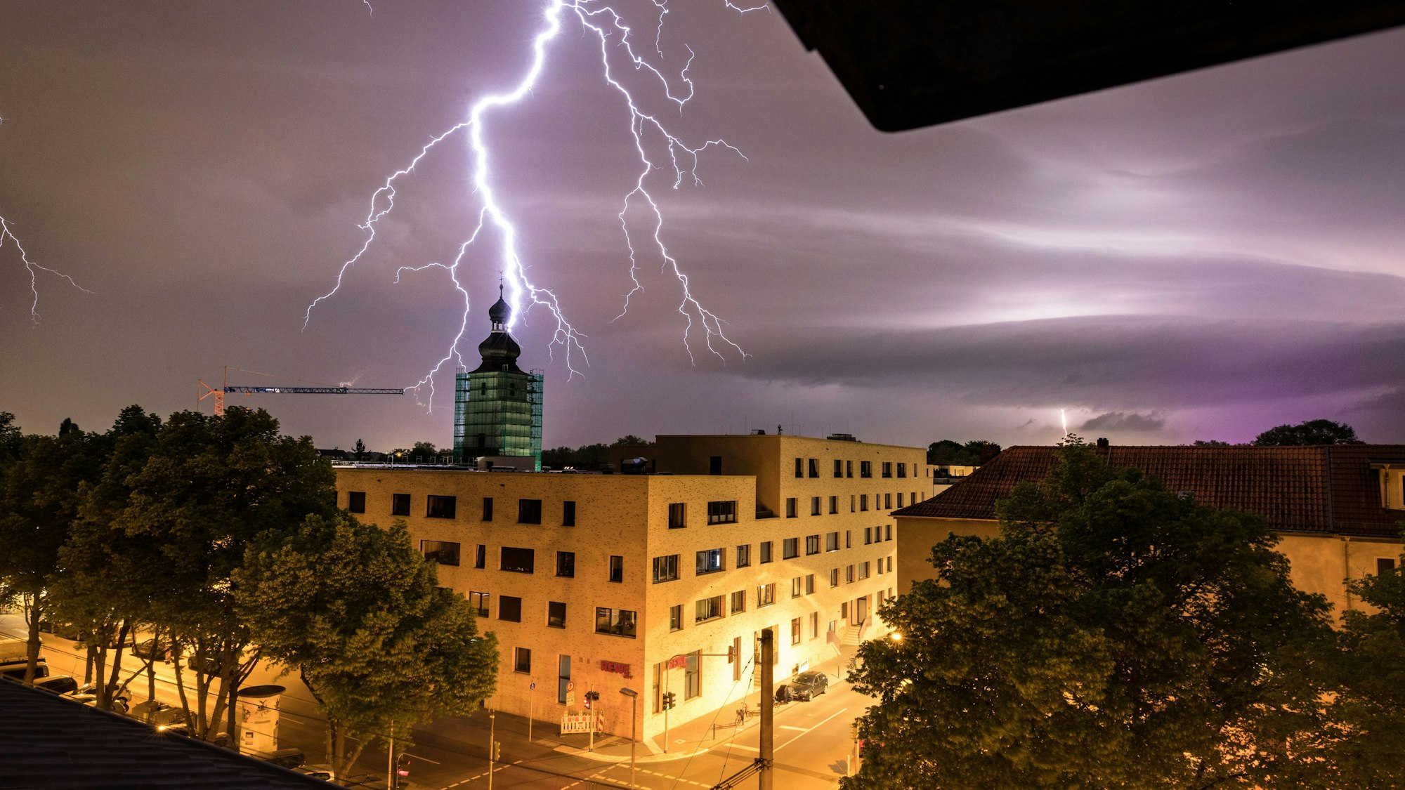 Hinter dem Kirchturm der Kirche "Zur heiligen Familie“i n Köln schlägt ein Blitz ein.